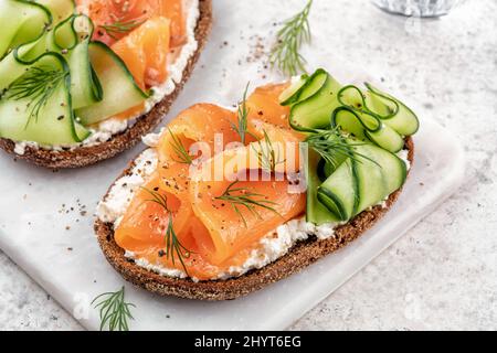 Roggenbrot öffnet Sandwiches mit gesalzenem Lachs und Gurke auf einem Tisch aus weißem Stein. Gesunde Ernährung. Stockfoto