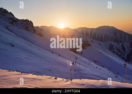 Wunderschöne Landschaft Shymbulak Mountain Resort schneebedeckten leeren Skipiste und Seilbahn bei Sonnenuntergang orange Himmel leuchten in Almaty, Kasachstan. Stockfoto