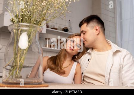 Glückliches Paar sitzt am Küchentisch, träumt, umarmt. Schöne Frau und schöner Mann verbringen Zeit zusammen und reden zu Hause. Hochwertige Fotos Stockfoto