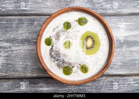 Joghurt mit Kiwi, Stachelbeere, Chia und Mandeln in Holzschüssel auf grauem Holzgrund. Draufsicht, flach liegend, Nahaufnahme. Stockfoto