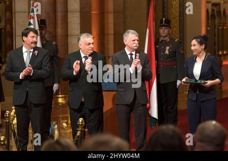 (220315) -- BUDAPEST, 15. März 2022 (Xinhua) -- Der ungarische Präsident Janos Ader, der Premierminister Viktor Orban und der Parlamentspräsident Laszlo Kover (1. bis 3. Liter) applaudieren Zhang Jing, Cheftrainer des ungarischen Kurzstrecken-Eisschnelllaufteams, während einer Preisverleihung vor dem Nationalfeiertag in Budapest, Ungarn, am 14. März 2022. Zhang Jing erhielt das mittlere Kreuz des Verdienstordens von Ungarn in Anerkennung ihrer sportlichen Bemühungen bei den Olympischen Winterspielen in Peking. (Foto von Attila Volgyi/Xinhua) Stockfoto