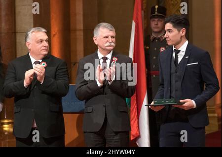 (220315) -- BUDAPEST, 15. März 2022 (Xinhua) -- der ungarische Premierminister Viktor Orban (1. L) und der Parlamentspräsident Laszlo Kover (C) applaudieren dem Kurzstrecken-Eisschnellläufer Shaoang Liu (R) während einer Preisverleihung vor dem Nationalfeiertag in Budapest, Ungarn, 14. März 2022. Shaoang Liu wurde in Anerkennung seiner sportlichen Bemühungen bei den Olympischen Winterspielen in Peking mit dem Mittelkreuz des Verdienstordens von Ungarn ausgezeichnet. (Foto von Attila Volgyi/Xinhua) Stockfoto