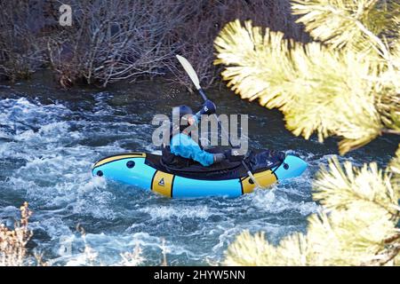 Ein Mann in einem trockenen Anzug, um ihn vor dem kalten Kajak auf dem Deschutes River in Oregon in einem kleinen Kajak zu schützen. Stockfoto