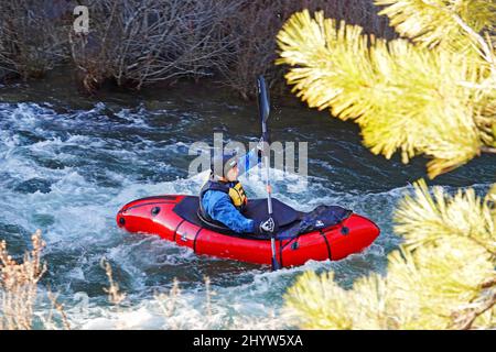 Ein Mann in einem trockenen Anzug, um ihn vor dem kalten Kajak auf dem Deschutes River in Oregon in einem kleinen Kajak zu schützen. Stockfoto