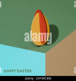 Der Text Happy easter und ein osterei auf dünnem Sperrholz, das in verschiedenen Farben lackiert ist, auf einer grünen, braunen und blauen Oberfläche, die ein visuelles illu erzeugt, ausgeschnitten Stockfoto