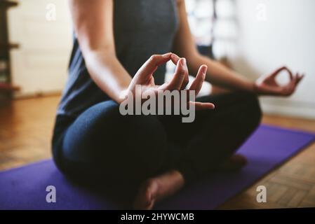 Mein Gleichgewicht finden. Eine kurze Aufnahme einer unkenntlichen Frau, die auf einer Yogamatte sitzt und allein in ihrem Haus meditiert. Stockfoto