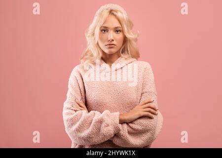 Serious stylish Dame Blick auf die Kamera und posiert mit gefalteten Armen über rosa Studio Hintergrund Stockfoto