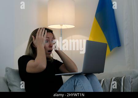 Eine junge, ängstliche Frau mit ausschreienden Augen las die Nachrichten über die Ukraine auf ihrem Laptop. Nahaufnahme, Kopierbereich, Hintergrund. Stockfoto