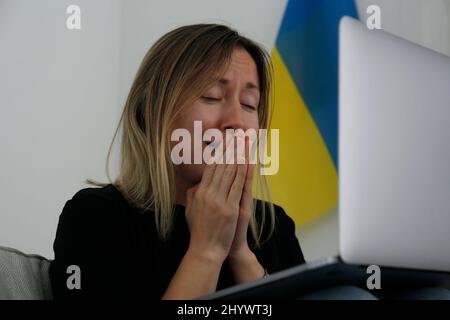 Eine junge, ängstliche Frau mit ausschreienden Augen las die Nachrichten über die Ukraine auf ihrem Laptop. Nahaufnahme, Kopierbereich, Hintergrund. Stockfoto