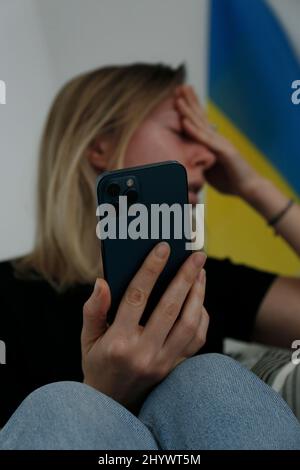 Eine junge, ängstliche Frau mit weinenden Augen las die Nachrichten über die Ukraine auf ihrem Handy. Nahaufnahme, Kopierbereich, Hintergrund. Stockfoto