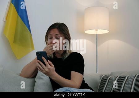 Eine junge, ängstliche Frau mit weinenden Augen las die Nachrichten über die Ukraine auf ihrem Handy. Nahaufnahme, Kopierbereich, Hintergrund. Stockfoto