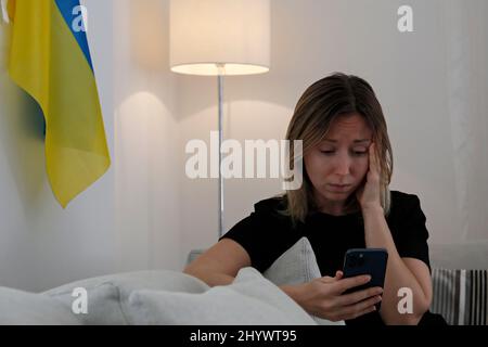 Eine junge, ängstliche Frau mit weinenden Augen las die Nachrichten über die Ukraine auf ihrem Handy. Nahaufnahme, Kopierbereich, Hintergrund. Stockfoto