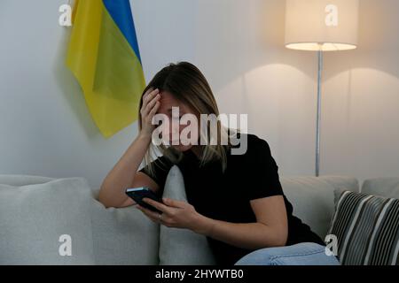 Eine junge, ängstliche Frau mit weinenden Augen las die Nachrichten über die Ukraine auf ihrem Handy. Nahaufnahme, Kopierbereich, Hintergrund. Stockfoto