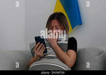 Eine junge, ängstliche Frau mit weinenden Augen las die Nachrichten über die Ukraine auf ihrem Handy. Nahaufnahme, Kopierbereich, Hintergrund. Stockfoto