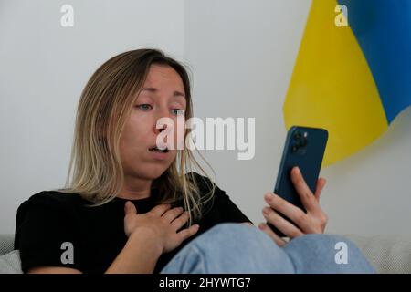 Eine junge, ängstliche Frau mit weinenden Augen las die Nachrichten über die Ukraine auf ihrem Handy. Nahaufnahme, Kopierbereich, Hintergrund. Stockfoto