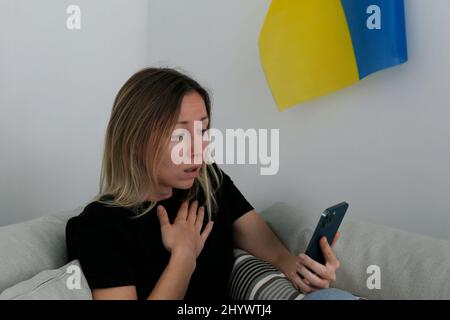 Eine junge, ängstliche Frau mit weinenden Augen las die Nachrichten über die Ukraine auf ihrem Handy. Nahaufnahme, Kopierbereich, Hintergrund. Stockfoto