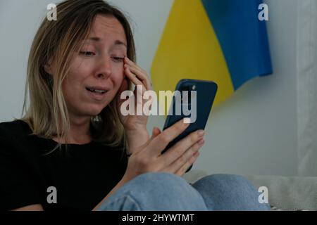 Eine junge, ängstliche Frau mit weinenden Augen las die Nachrichten über die Ukraine auf ihrem Handy. Nahaufnahme, Kopierbereich, Hintergrund. Stockfoto