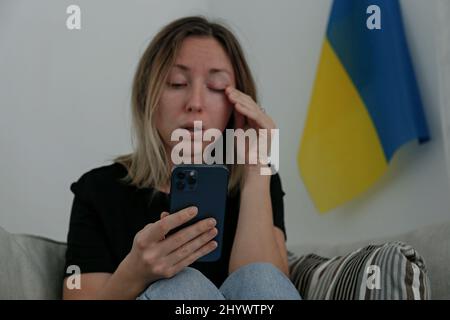 Eine junge, ängstliche Frau mit weinenden Augen las die Nachrichten über die Ukraine auf ihrem Handy. Nahaufnahme, Kopierbereich, Hintergrund. Stockfoto