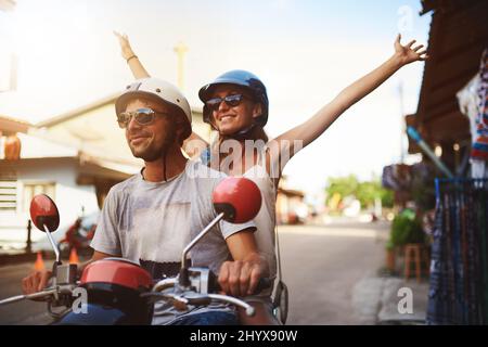 Genießen Sie einfach die Fahrt. Aufnahme von jungen Touristen, die eine Motorroller-Fahrt durch die Stadt genießen. Stockfoto