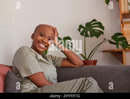 Eine junge Frau schaut direkt auf die Kamera, die zu Hause auf der Couch sitzt Stockfoto
