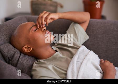 Eine junge Frau liegt auf der Couch und hält ihre Nase wegen Verstopfung und Schmerzen Stockfoto