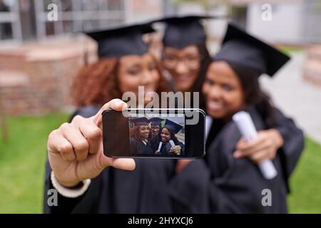 Erinnerungen an monumentale Momente. Aufnahme von drei weiblichen Absolventen, die am Telefon ein Bild von sich selbst machen. Stockfoto