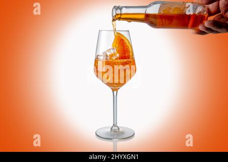 Alkoholischer Aperol Spritz Cocktail aus Glasflasche in Glas mit Eiswürfel und orangefarbener Scheibe gegossen, weißes Licht auf orangefarbenem Hintergrund Stockfoto