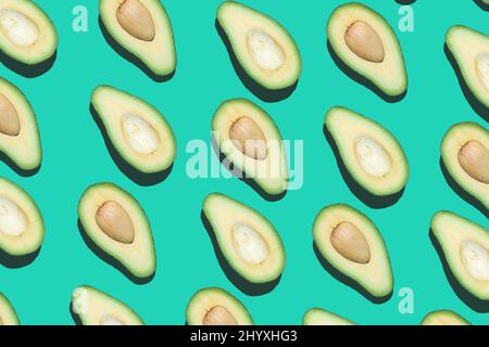 Grafisches Draufsicht-Muster von Avocado-Hälften in diagonalen Linien auf kontrastierenden blauen Hintergrund, gesundes Essen und veganes Konzept, Kopierraum Stockfoto