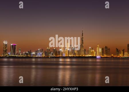 Die Skyline der Dubai Business Bay bei Nacht mit farbenfrohen, beleuchteten Gebäuden und dem ruhigen Wasser des Dubai Creek. Stockfoto