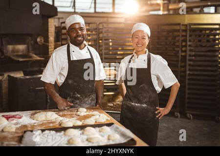 Porträt von lächelnden, multirassischen Bäckerinnen mit mittlerem Erwachsenenalter, die in der Bäckerei stehen Stockfoto