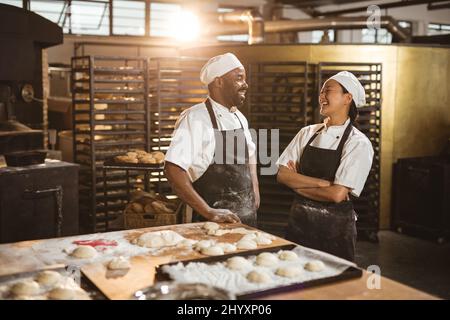 Lächelnde, mehrrassige Bäckerinnen und -Bäcker mit mittlerem Erwachsenenalter reden, während sie in der Bäckerei stehen Stockfoto