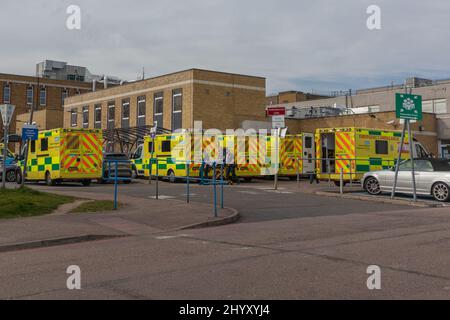 Southend on Sea, Großbritannien. März 2022. Eine Reihe gelber und grüner Rettungswagen, die in einem ausgewiesenen Bereich vor einem mehrstöckigen Krankenhausgebäude in Southend, Großbritannien, geparkt sind. Die Szene zeigt die Bereitschaft und Infrastruktur des NHS für medizinische Notdienste, mit sichtbaren Schildern, Zufahrtsstraßen und Gesundheitsarchitektur. Krankenwagen warten vor dem Southend University Hospital, da die Nachfrage nach Dienstleistungen im Krankenhaus weiterhin extrem hoch ist. Penelope Barritt/Alamy Live News Stockfoto