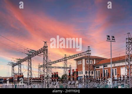 Elektrische Transformatorstation mit Pylonen mit Hochspannungskabeln, farbenprächtiger Sonnenuntergang, teures Energiekostenkonzept Stockfoto