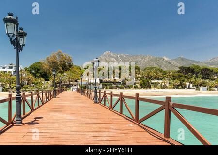 Blick auf die rote Holzbrücke 'Embarcadero' in Marbella. Blick auf das Luxusgebiet Puente Romano, teure Urbanisationen. Berg „La Concha“. Stockfoto