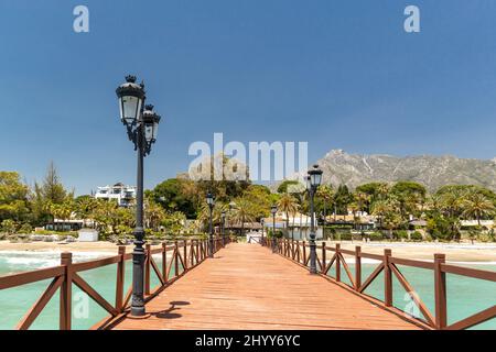 Blick auf die rote Holzbrücke 'Embarcadero' in Marbella. Blick auf das Luxusgebiet Puente Romano, teure Urbanisationen. Berg „La Concha“. Stockfoto