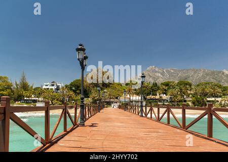 Blick auf die rote Holzbrücke 'Embarcadero' in Marbella. Blick auf das Luxusgebiet Puente Romano, teure Urbanisationen. Berg „La Concha“. Stockfoto