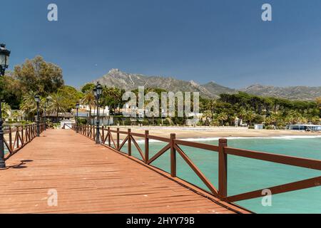 Blick auf die rote Holzbrücke 'Embarcadero' in Marbella. Blick auf das Luxusgebiet Puente Romano, teure Urbanisationen. Berg „La Concha“. Stockfoto