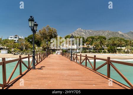 Blick auf die rote Holzbrücke 'Embarcadero' in Marbella. Blick auf das Luxusgebiet Puente Romano, teure Urbanisationen. Berg „La Concha“. Stockfoto