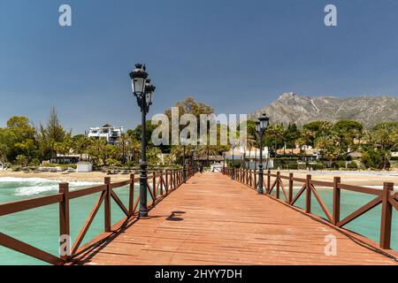 Blick auf die rote Holzbrücke 'Embarcadero' in Marbella. Blick auf das Luxusgebiet Puente Romano, teure Urbanisationen. Berg „La Concha“. Stockfoto