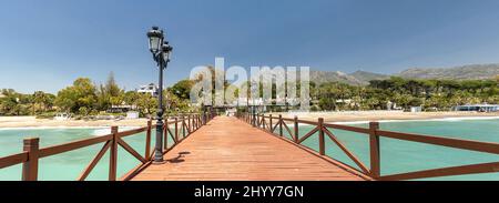 Blick auf die rote Holzbrücke 'Embarcadero' in Marbella. Blick auf das Luxusgebiet Puente Romano, teure Urbanisationen. Berg „La Concha“. Stockfoto