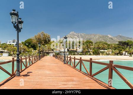 Blick auf die rote Holzbrücke 'Embarcadero' in Marbella. Blick auf das Luxusgebiet Puente Romano, teure Urbanisationen. Berg „La Concha“. Stockfoto