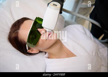 ELOS Epilation Haarentfernung auf dem Gesicht einer schönen Frau. Kosmetikerin, die Laser-Verjüngung in einem Schönheitssalon macht. Gesichtspflege. Hardw Stockfoto