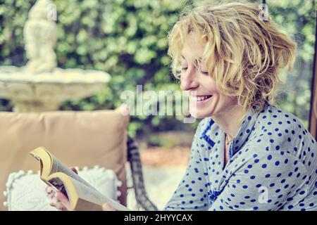 Porträt einer jungen reifen kaukasischen Frau drinnen zu Hause, die ein Buch liest. Quarantänekonzept. Stockfoto