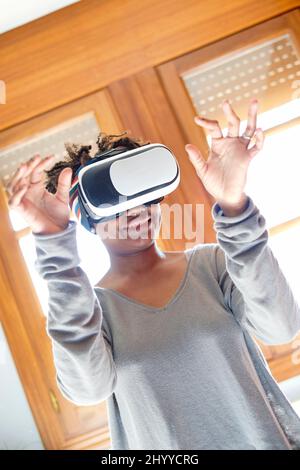 Porträt einer aktiven jungen schwarzen Frau, die einen Virtual-Reality-Simulator in einem Raum zu Hause testet. Technologie- und Lifestyle-Konzepte. Stockfoto