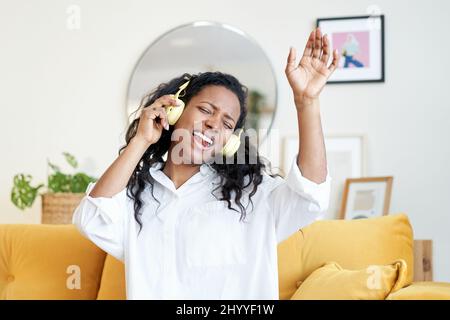 Motivierte junge Lateinerin, die mit Kopfhörern Musik hört, während sie zu Hause auf dem Sofa sitzt. Stockfoto