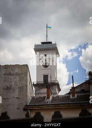 Ukrainische Flagge auf der Spitze des Rathausturms in Lemberg, Ukraine, mit bewölktem Hintergrund. Lviv ist die Hauptstadt der Westukraine und das Rathaus Stockfoto