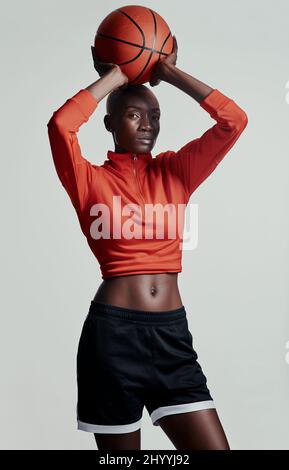 Zielen, schießen, Punkten. Studioaufnahme einer attraktiven jungen Frau, die vor grauem Hintergrund Basketball spielt. Stockfoto