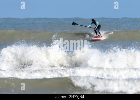 Eine ältere weibliche Stand-up-Paddleboard-Surferin, die am Boca Chica Beach in der Nähe von Brownsville, Texas, eine Welle erhakt. Stockfoto