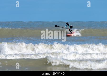 Eine ältere weibliche Stand-up-Paddleboard-Surferin, die am Boca Chica Beach in der Nähe von Brownsville, Texas, eine Welle erhakt. Stockfoto