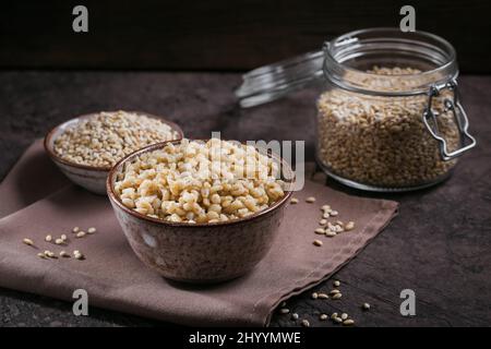 Schmackhafter Getreidebrei aus Perlgerste in einer Schüssel auf dunklem Hintergrund. Gesunde Ernährung und Konzept der Ernährung. Stockfoto